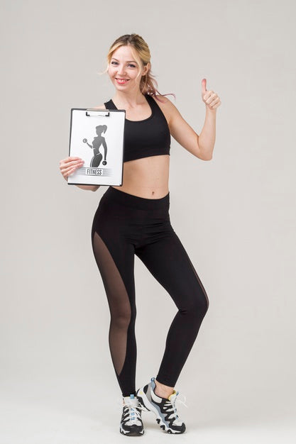 Front View Of Smiley Fitness Woman Holding Notepad And Giving Thumbs Up Psd