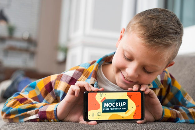 Front View Of Smiley Kid On Couch Holding Smartphone Psd