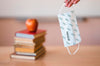 Front View Of Teacher Holding Medical Mask With Books And Apple Psd