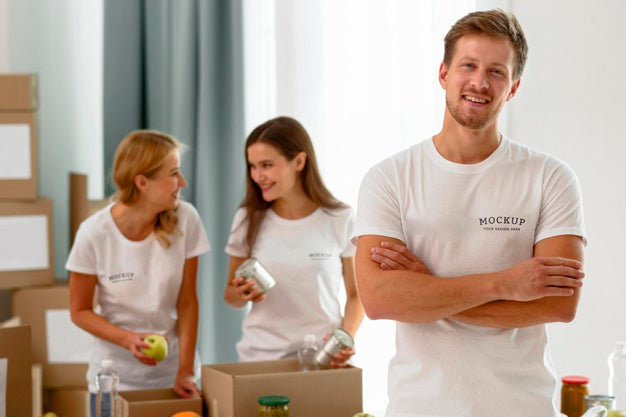 Male Volunteer Posing With Arms Crossed While Colleagues Prepare Donation Boxes Psd