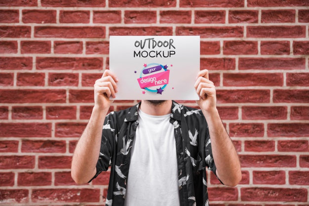 Man Presenting Poster Mockup In Front Of Brick Wall Psd