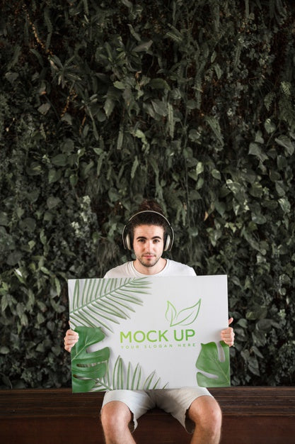 Man Presenting Poster Mockup In Front Of Leaves Psd