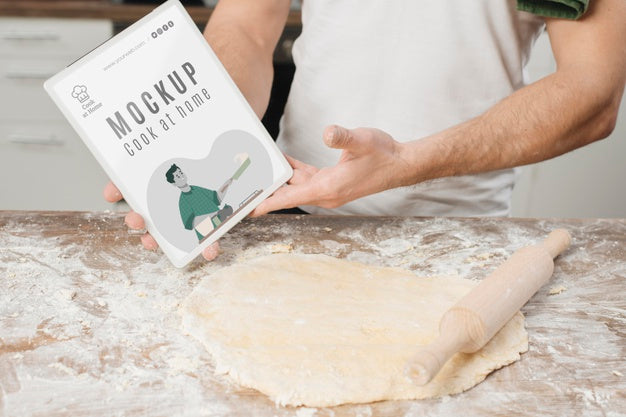 Man Rolling Dough In The Kitchen And Holding Book Psd