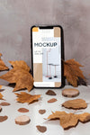 Mobile Phone Mockup Standing On The Table Surrounded By Leaves Psd