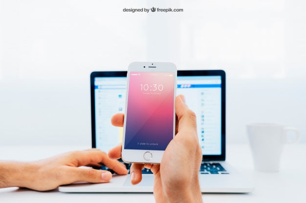 Mockup Of Hand Holding Smartphone In Front Of Laptop Psd