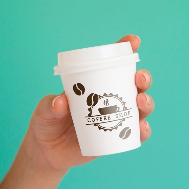 Person Holding Up A Coffee Paper Cup On Blue Background Psd