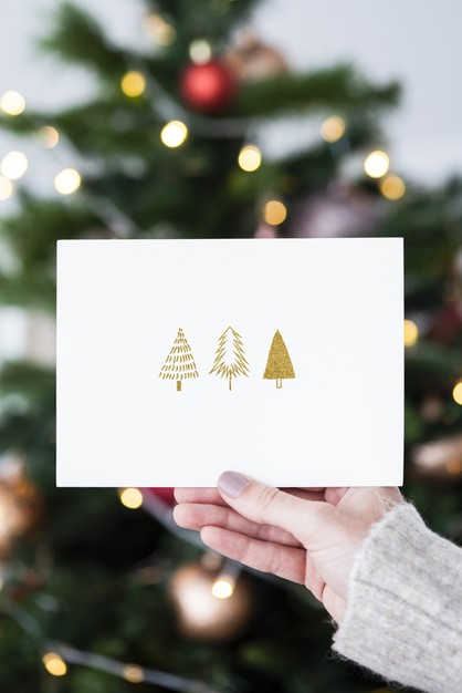 Woman Holding A Christmas Card In Front Of A Christmas Tree Mockup Psd