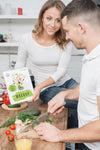 Woman Holding Book In The Kitchen While Man Cooks Psd